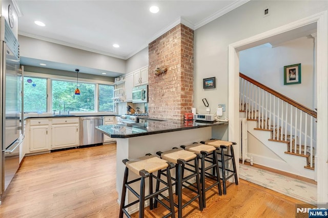 kitchen with stainless steel appliances, a peninsula, white cabinets, light wood-style flooring, and crown molding