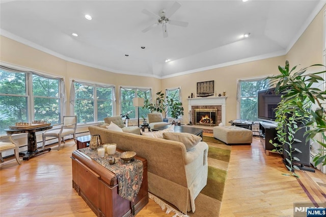 living area featuring a ceiling fan, a glass covered fireplace, light wood-style floors, ornamental molding, and recessed lighting