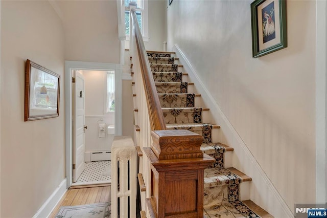 staircase with wood finished floors, a baseboard radiator, and baseboards