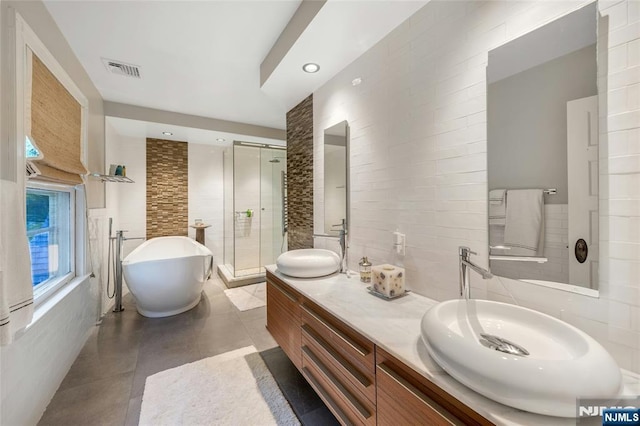 bathroom with tile walls, a shower stall, a soaking tub, double vanity, and recessed lighting