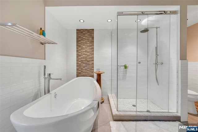 full bathroom with tile walls, a stall shower, a freestanding tub, a sink, and toilet