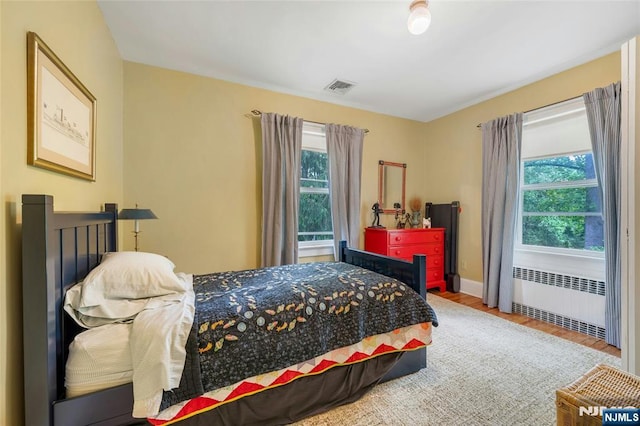 bedroom with radiator heating unit, wood finished floors, and baseboards