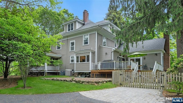 back of house with central AC unit, a deck, and a chimney