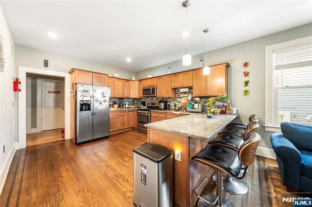 kitchen with appliances with stainless steel finishes, a peninsula, wood finished floors, pendant lighting, and baseboards