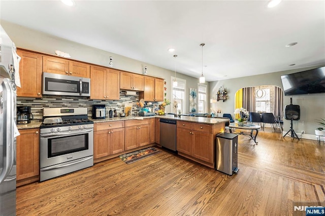 kitchen with appliances with stainless steel finishes, arched walkways, a peninsula, dark wood-style floors, and decorative backsplash