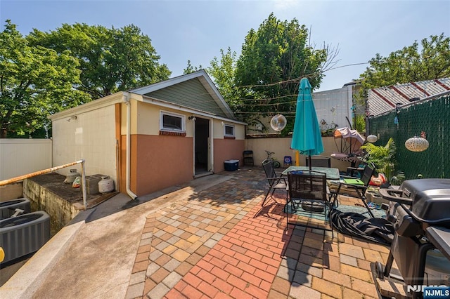 view of patio / terrace featuring a fenced backyard, outdoor dining area, an outbuilding, and central AC unit