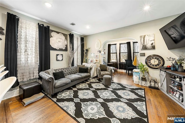 living room with arched walkways, wood finished floors, and recessed lighting