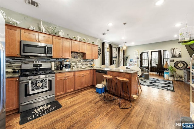 kitchen featuring appliances with stainless steel finishes, wood finished floors, backsplash, a sink, and a peninsula