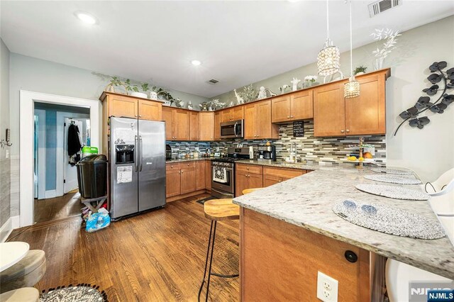 kitchen with stainless steel appliances, dark wood-type flooring, a sink, brown cabinetry, and a peninsula
