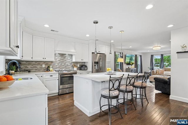 kitchen featuring stainless steel appliances, premium range hood, a sink, a breakfast bar, and dark wood finished floors