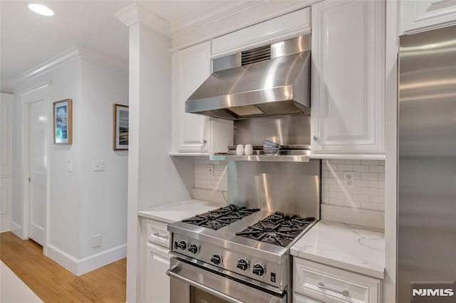 kitchen with premium appliances, wall chimney range hood, white cabinetry, light stone counters, and decorative backsplash