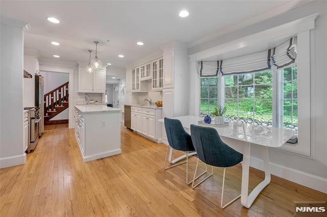 kitchen with ornamental molding, light countertops, white cabinets, stainless steel appliances, and a kitchen island