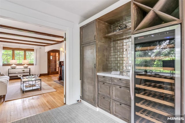 bar area featuring arched walkways, wine cooler, light wood-style floors, and baseboards