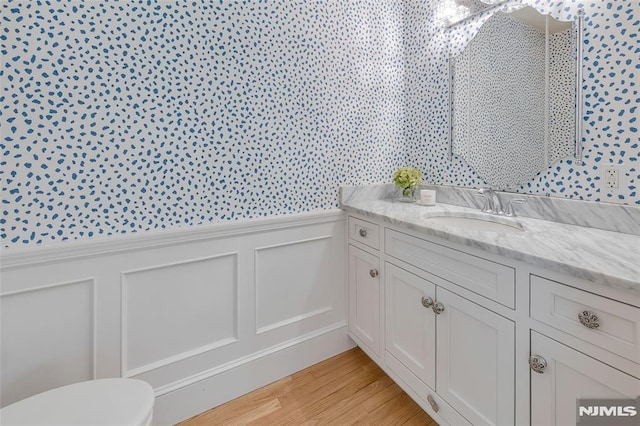 bathroom featuring wainscoting, a decorative wall, vanity, toilet, and wood finished floors