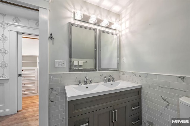 bathroom with tile walls, vanity, a wainscoted wall, wood finished floors, and toilet