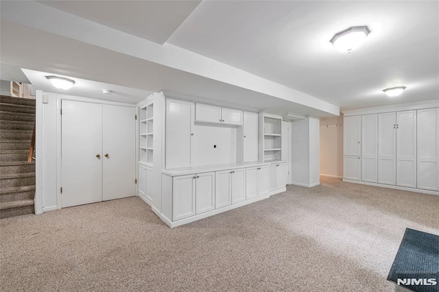 finished below grade area featuring light carpet, stairs, and baseboards