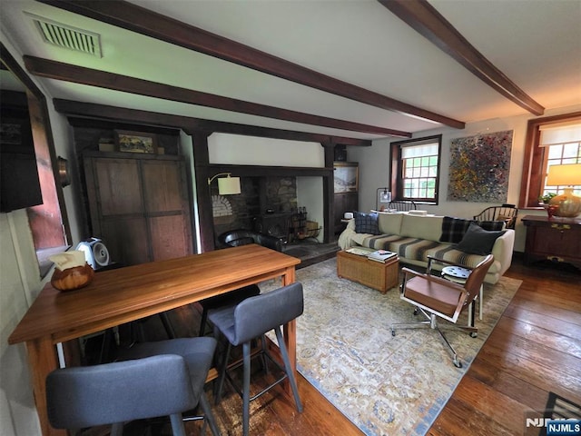 living room featuring beam ceiling, wood-type flooring, and a wood stove