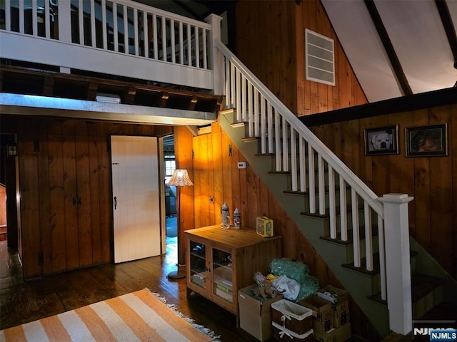 staircase with wooden walls, wood-type flooring, and high vaulted ceiling