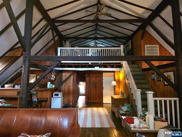 unfurnished living room featuring ceiling fan, wood walls, wood finished floors, and high vaulted ceiling