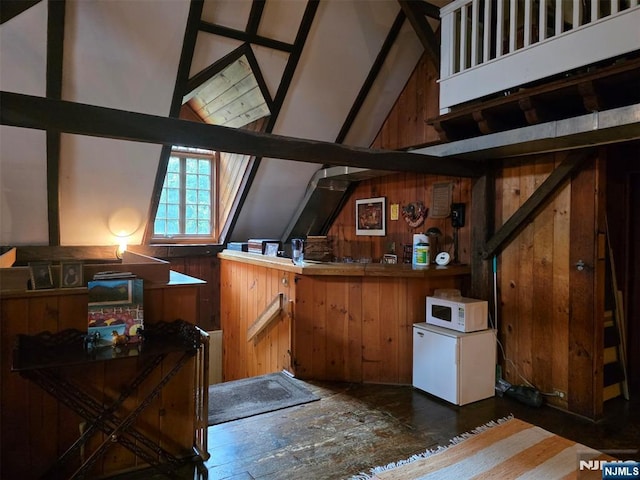 bar area with white microwave, wood walls, refrigerator, and vaulted ceiling