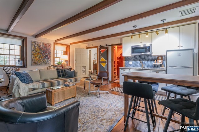 living room featuring a barn door, beamed ceiling, and wood finished floors
