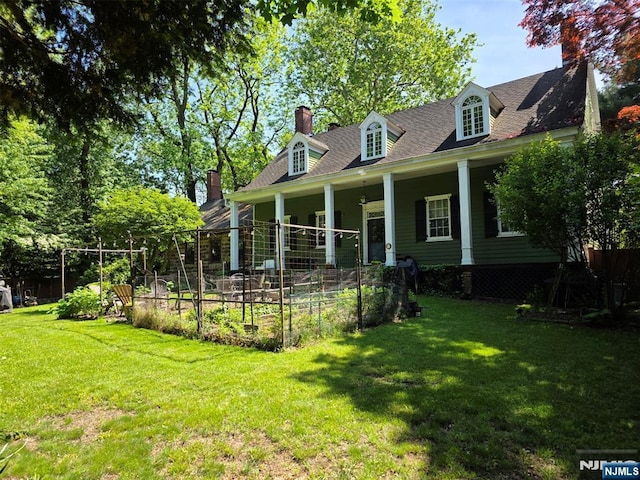 cape cod home featuring a garden, a front lawn, a chimney, and roof with shingles