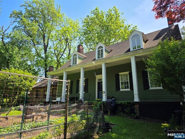 cape cod house featuring a chimney, a porch, a vegetable garden, and a shingled roof