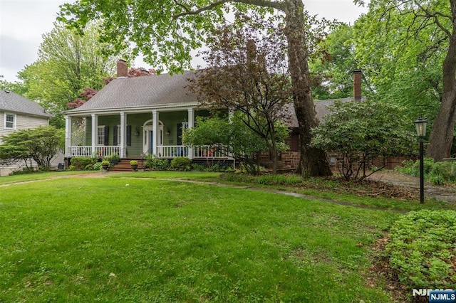 view of front of property featuring a chimney, covered porch, and a front yard