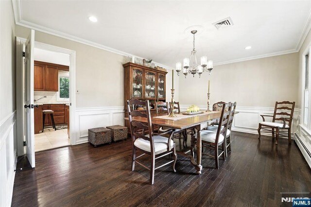 dining space featuring a chandelier, dark wood-style floors, ornamental molding, a wainscoted wall, and a decorative wall