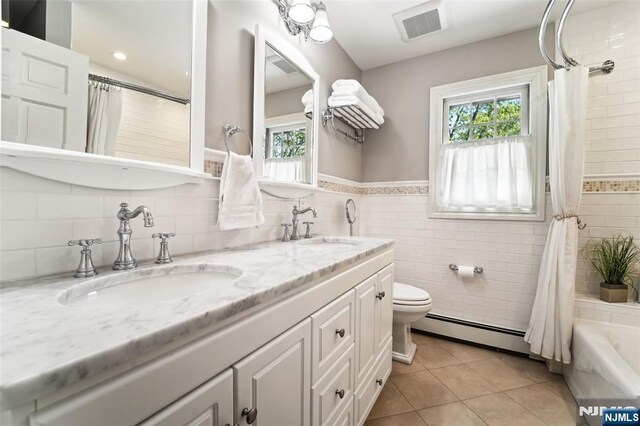 full bathroom featuring a baseboard heating unit, tile patterned floors, tile walls, toilet, and double vanity