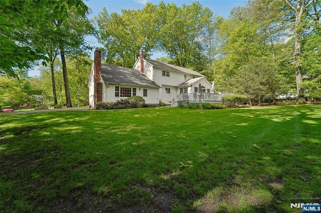 rear view of property featuring a yard, a wooden deck, and a chimney