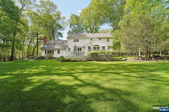 rear view of house with a chimney, a lawn, and a wooden deck