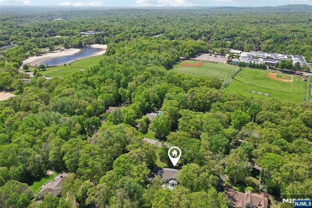 aerial view of property and surrounding area featuring a heavily wooded area and a nearby body of water