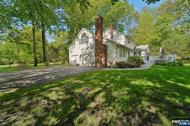 view of home's exterior with asphalt driveway, an attached garage, a chimney, a yard, and a deck