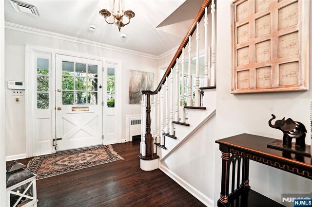 entrance foyer with dark wood-type flooring, stairs, ornamental molding, a chandelier, and radiator