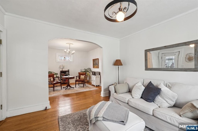 living area with arched walkways, a chandelier, crown molding, wood finished floors, and baseboards