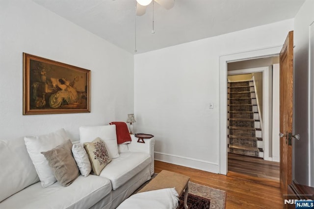 living area with wood finished floors, a ceiling fan, stairway, and baseboards