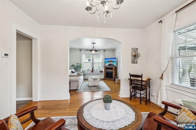 living room with arched walkways, wood finished floors, crown molding, a chandelier, and baseboards
