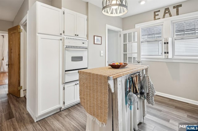 kitchen with white oven, a warming drawer, white cabinetry, and light wood-style floors