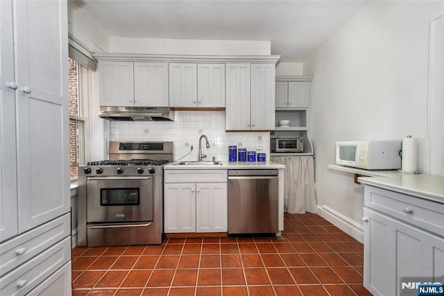 kitchen featuring appliances with stainless steel finishes, a sink, under cabinet range hood, tasteful backsplash, and dark tile patterned floors