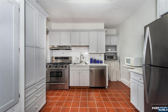 kitchen featuring appliances with stainless steel finishes, a sink, under cabinet range hood, decorative backsplash, and dark tile patterned floors