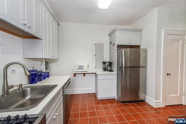 kitchen featuring appliances with stainless steel finishes, a sink, baseboards, dark tile patterned floors, and decorative backsplash