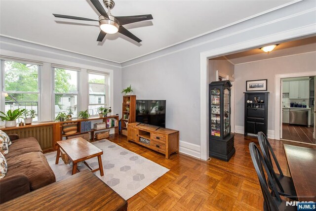 living room featuring a ceiling fan, baseboards, and crown molding