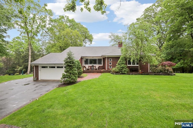 view of front of property with driveway, a chimney, an attached garage, a front lawn, and brick siding