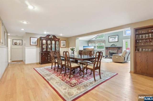 dining room with light wood-type flooring, a fireplace, wainscoting, and recessed lighting
