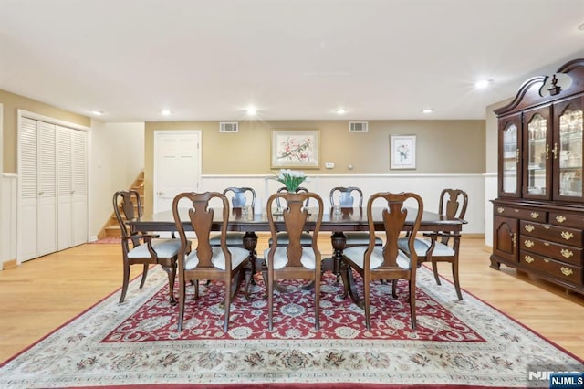 dining room featuring light wood-style floors, wainscoting, and stairway