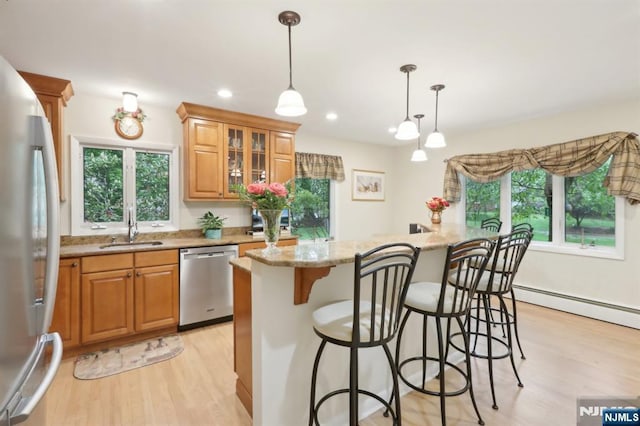 kitchen featuring stainless steel dishwasher, refrigerator, a sink, light wood-style floors, and a kitchen bar