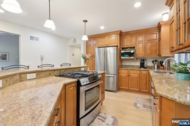 kitchen with stainless steel appliances, a sink, light wood-type flooring, light stone countertops, and pendant lighting