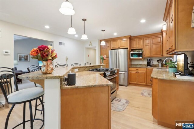 kitchen with appliances with stainless steel finishes, light wood-type flooring, a breakfast bar, a sink, and a center island with sink