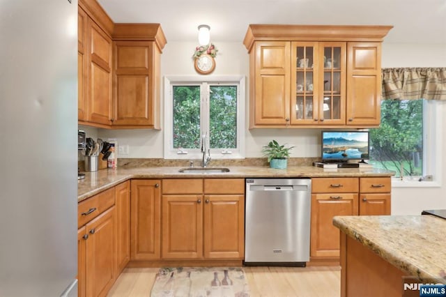 kitchen featuring stainless steel dishwasher, a sink, freestanding refrigerator, light stone countertops, and glass insert cabinets